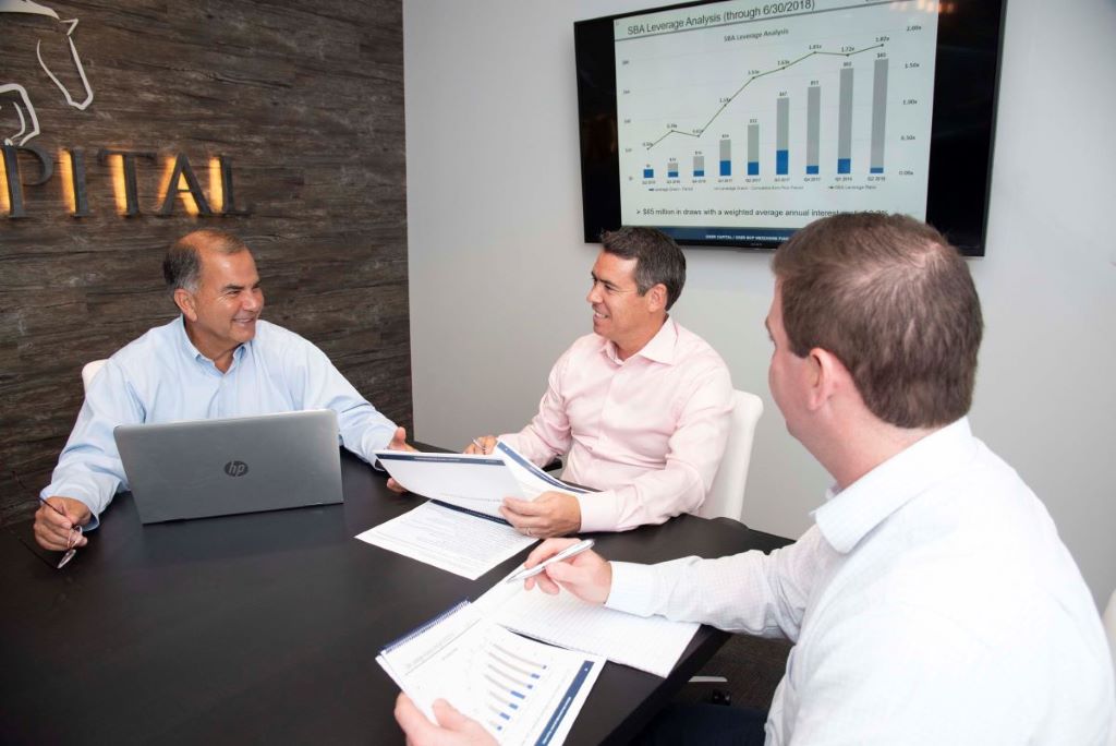 Three men sit at a conference table