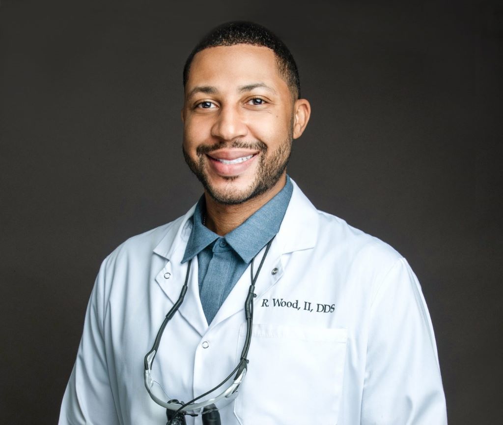 a smiling doctor in a white lab coat in front of a dark gray background